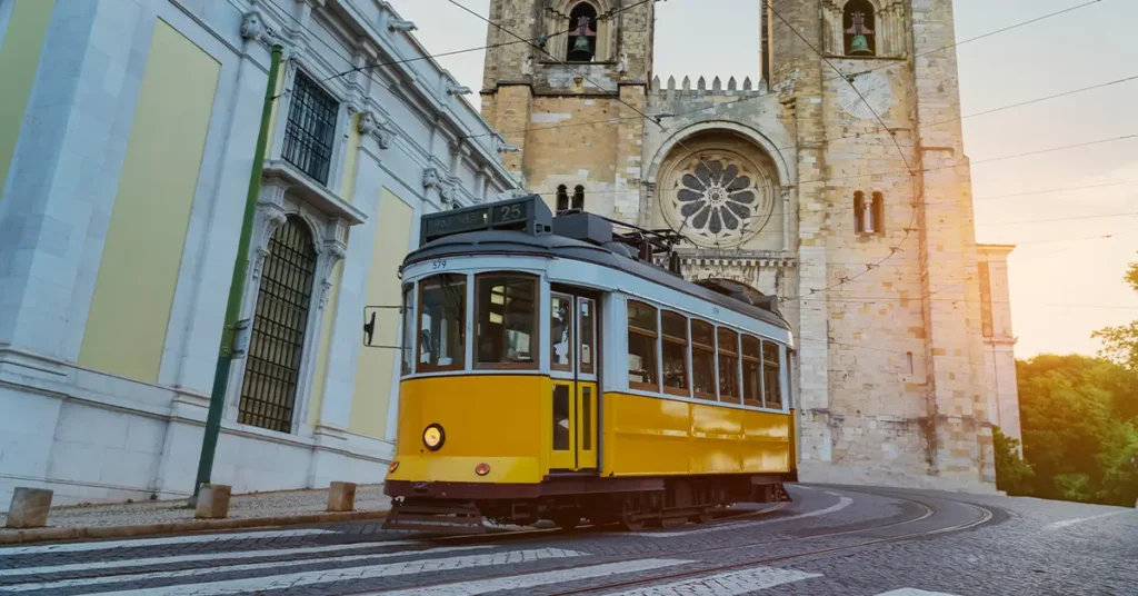 Typical yellow tram going up the Alfama district in front of Lisbon cathedral Portugal