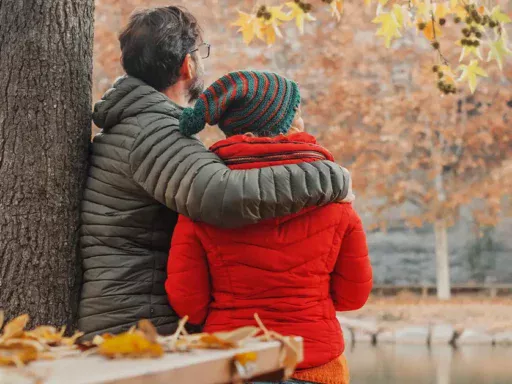 Dating couple viewed from back enjoy scenic view at the lake in autumn winter day Love and relationship Romantic moment for man and woman hugging and enjoying outdoor leisure activity together